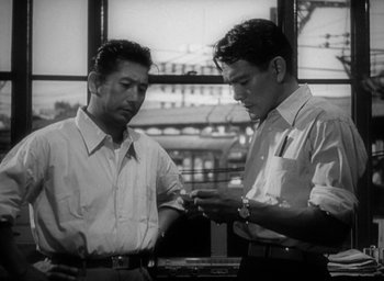 Movie still from “Godzilla” (1954), directed by Ishirô Honda – Two men are looking at a cell phone; Medium shot, Low angle