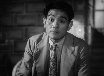 Movie still from “Godzilla” (1954), directed by Ishirô Honda – A man wearing a suit and tie sitting in front of a brick wall; Close Up shot, Low angle