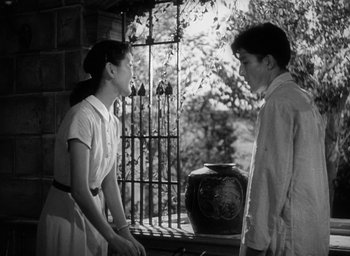 Movie still from “Godzilla” (1954), directed by Ishirô Honda – A young man and a young woman standing next to each other in front of an urn; Medium shot, Low angle