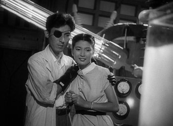 Movie still from “Godzilla” (1954), directed by Ishirô Honda – A man and a woman posing for a picture in an industrial setting; Medium shot, Low angle