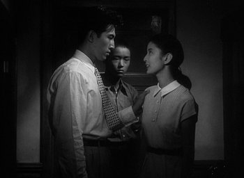 Movie still from “Godzilla” (1954), directed by Ishirô Honda – A man and a woman talking to another man in front of another woman; Medium shot, Low angle