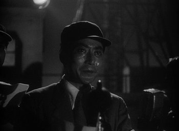 Movie still from “Godzilla” (1954), directed by Ishirô Honda – A man wearing a hat and a suit is looking at the camera; Close Up shot, Low angle