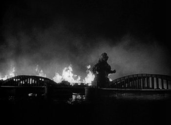 Movie still from “Godzilla” (1954), directed by Ishirô Honda – A person standing in front of a bridge on fire; Extreme Wide shot, Low angle