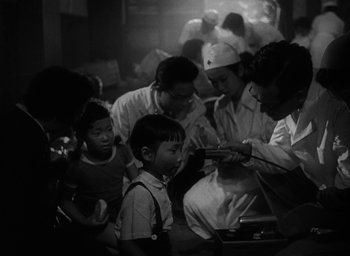 Movie still from “Godzilla” (1954), directed by Ishirô Honda – A group of people gathered in a room; Medium shot, High angle