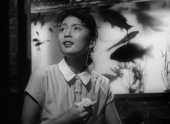 Movie still from “Godzilla” (1954), directed by Ishirô Honda – An asian woman holding a flower in her hand; Medium shot, Low angle