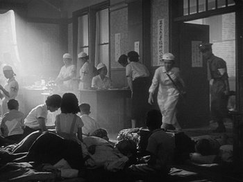 Movie still from “Godzilla: King of the Monsters!” (1956), directed by Ishirô Honda – A black and white photo of a group of people in a room; Wide shot, High angle