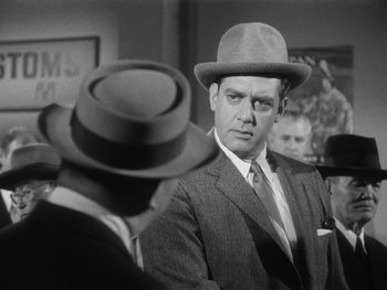 Movie still from “Godzilla: King of the Monsters!” (1956), directed by Ishirô Honda – A black and white photo of a man in a suit and a hat; Medium shot, Over the shoulder angle