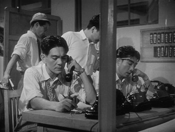 Movie still from “Godzilla: King of the Monsters!” (1956), directed by Ishirô Honda – A group of men sitting at a table talking to each other; Medium shot, High angle
