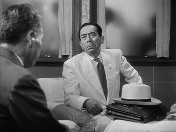 Movie still from “Godzilla: King of the Monsters!” (1956), directed by Ishirô Honda – A man sitting on a couch talking to another man in a suit; Medium shot, Over the shoulder angle