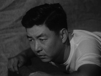 Movie still from “Godzilla: King of the Monsters!” (1956), directed by Ishirô Honda – An asian man looking down while sitting on the ground; Close Up shot, High angle