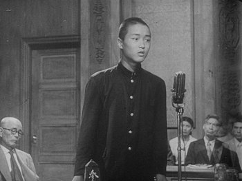 Movie still from “Godzilla: King of the Monsters!” (1956), directed by Ishirô Honda – An old photo of a young man in a courtroom; Medium shot, Over the shoulder angle