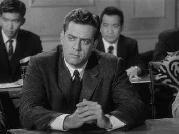 Movie still from “Godzilla: King of the Monsters!” (1956), directed by Ishirô Honda – A black and white photo of a man sitting at a table; Medium shot, Low angle