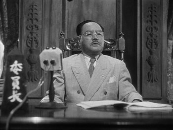 Movie still from “Godzilla: King of the Monsters!” (1956), directed by Ishirô Honda – An older man sitting at a desk in front of a mirror; Medium shot, Low angle