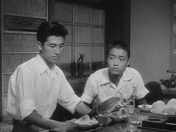 Movie still from “Godzilla: King of the Monsters!” (1956), directed by Ishirô Honda – Two young men are sitting at a table with food; Medium shot, Low angle