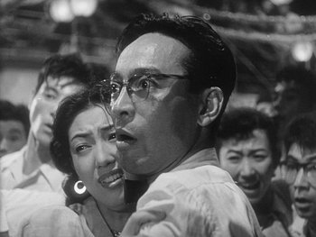 Movie still from “Godzilla: King of the Monsters!” (1956), directed by Ishirô Honda – A man and a woman are hugging in a crowd; Close Up shot, Low angle
