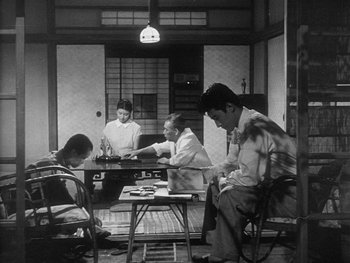 Movie still from “Godzilla: King of the Monsters!” (1956), directed by Ishirô Honda – A black and white photo of a group of people sitting around a table; Wide shot, High angle