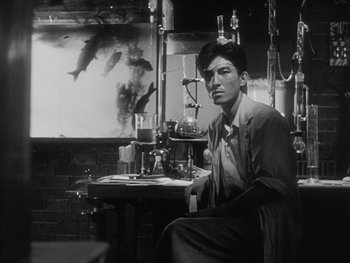 Movie still from “Godzilla: King of the Monsters!” (1956), directed by Ishirô Honda – A black and white photo of a man sitting at a table; Medium shot, Low angle