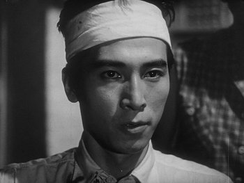 Movie still from “Godzilla: King of the Monsters!” (1956), directed by Ishirô Honda – A black and white photo of a man with a bandage on his head; Close Up shot, Low angle