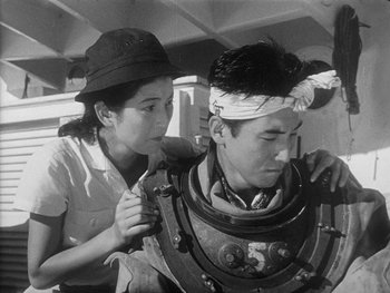 Movie still from “Godzilla: King of the Monsters!” (1956), directed by Ishirô Honda – A man and a woman are fixing a helmet on the back of a boat; Medium shot, High angle