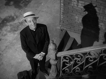 Movie still from “Going My Way” (1944), directed by Leo McCarey – A man in a hat standing on the steps of a fire hydrant; Medium shot, High angle