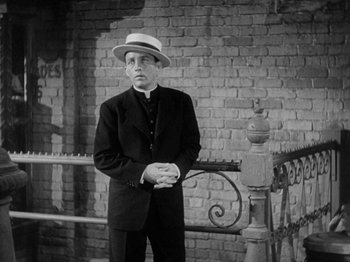 Movie still from “Going My Way” (1944), directed by Leo McCarey – A man wearing a suit and a hat standing in front of a brick wall; Medium shot, Low angle