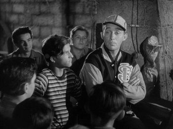 Movie still from “Going My Way” (1944), directed by Leo McCarey – A group of young men sitting in front of a brick wall; Medium shot, Over the shoulder angle