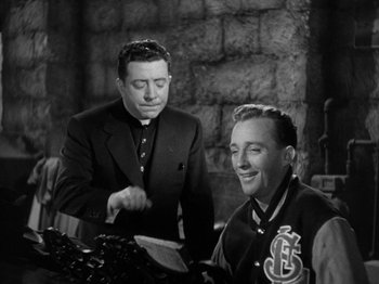 Movie still from “Going My Way” (1944), directed by Leo McCarey – Two men in suits are looking at a tablet computer; Medium shot, Low angle