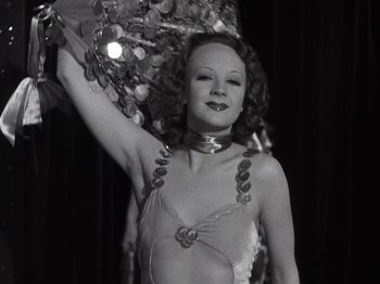 Movie still from “Gold Diggers of 1933” (1933), directed by Mervyn LeRoy – A black and white photo of a woman holding a fan; Medium shot, Low angle