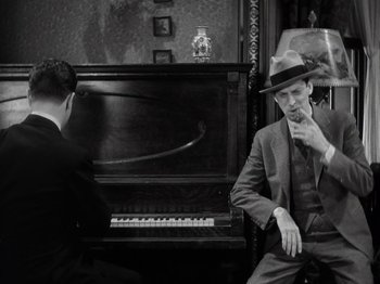 Movie still from “Gold Diggers of 1933” (1933), directed by Mervyn LeRoy – A man sitting next to another man in front of a piano; Medium shot, High angle