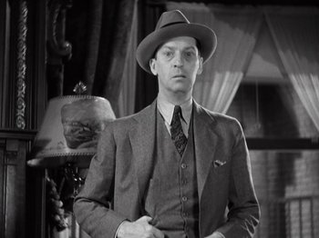 Movie still from “Gold Diggers of 1933” (1933), directed by Mervyn LeRoy – A man in a suit and hat standing in front of a lamp; Medium shot, Low angle