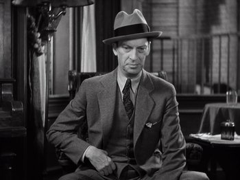 Movie still from “Gold Diggers of 1933” (1933), directed by Mervyn LeRoy – A man sitting in a chair wearing a suit and a hat; Close Up shot, Low angle