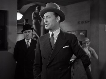 Movie still from “Gold Diggers of 1933” (1933), directed by Mervyn LeRoy – A man wearing a suit and hat while holding a briefcase; Medium shot, Low angle