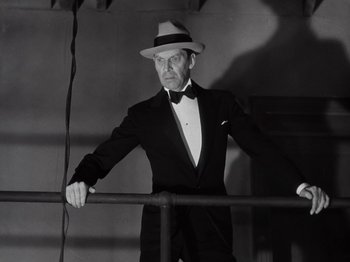 Movie still from “Gold Diggers of 1933” (1933), directed by Mervyn LeRoy – A man in a suit and hat leaning on a railing; Medium shot, Low angle