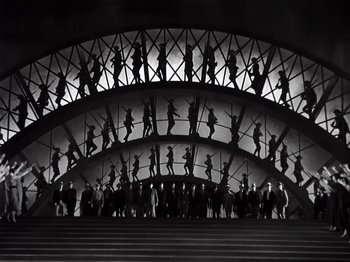 Movie still from “Gold Diggers of 1933” (1933), directed by Mervyn LeRoy – A black and white photo of a group of people standing in front of an archway; Extreme Wide shot, Low angle