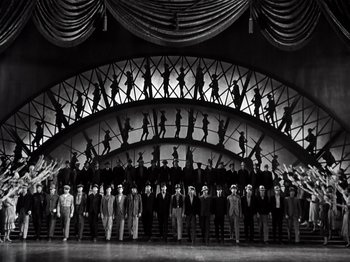 Movie still from “Gold Diggers of 1933” (1933), directed by Mervyn LeRoy – A black and white photo of a group of men standing in front of an audience; Extreme Wide shot, High angle