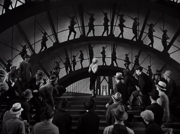 Movie still from “Gold Diggers of 1933” (1933), directed by Mervyn LeRoy – A group of people standing on steps in front of an audience; Wide shot, High angle