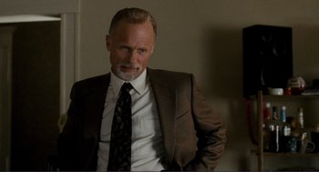 Movie still from “Gone Baby Gone” (2007), directed by Ben Affleck – A man in a suit and tie standing in front of a wall; Close Up shot, Low angle