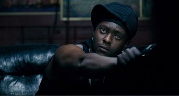 Movie still from “Gone Baby Gone” (2007), directed by Ben Affleck – A man in a black hat is sitting on a couch; Close Up shot, Low angle