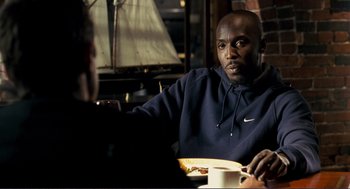 Movie still from “Gone Baby Gone” (2007), directed by Ben Affleck – A man sitting at a table with a plate of food; Medium shot, Over the shoulder angle