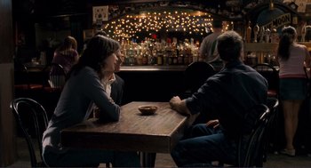 Movie still from “Gone Baby Gone” (2007), directed by Ben Affleck – Two people sitting at a table in front of a bar; Wide shot, Over the shoulder angle