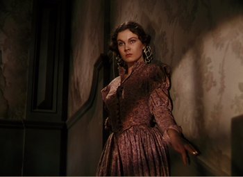 Movie still from “Gone with the Wind” (1939), directed by George Cukor – A woman in a dress standing next to a wall; Medium shot, Low angle