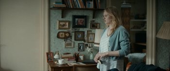 Movie still from “Graduation” (2016), directed by Cristian Mungiu – A woman standing in front of a wall with pictures on it; Medium shot, Over the shoulder angle