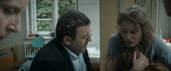 Movie still from “Graduation” (2016), directed by Cristian Mungiu – A person wearing glasses and a suit; Medium shot, Over the shoulder angle