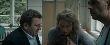 Movie still from “Graduation” (2016), directed by Cristian Mungiu – A man and a woman holding a baby in a room; Close Up shot, Over the shoulder angle