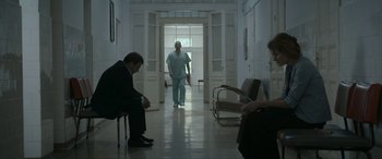 Movie still from “Graduation” (2016), directed by Cristian Mungiu – A man in a suit sitting on a chair in front of a doctor; Wide shot, Low angle
