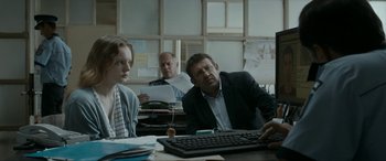 Movie still from “Graduation” (2016), directed by Cristian Mungiu – Three people sitting at a table with a computer keyboard; Medium shot, Over the shoulder angle