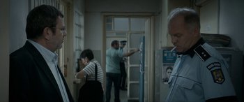 Movie still from “Graduation” (2016), directed by Cristian Mungiu – A group of people standing in front of a door; Medium shot, Over the shoulder angle
