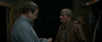 Movie still from “Graduation” (2016), directed by Cristian Mungiu – Two older men standing next to each other in a dark room; Medium shot, Over the shoulder angle