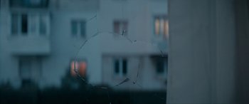 Movie still from “Graduation” (2016), directed by Cristian Mungiu – A broken glass window with a building in the background; Extreme Close Up shot, Over the shoulder angle