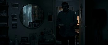 Movie still from “Graduation” (2016), directed by Cristian Mungiu – A man standing next to a teddy bear in the dark; Medium shot, Over the shoulder angle
